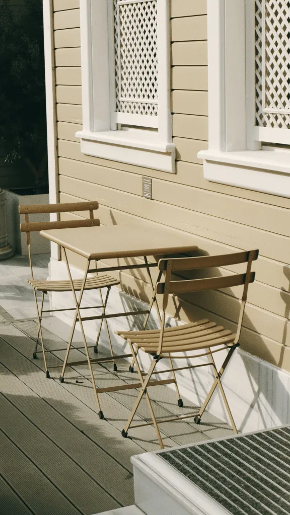 Bistro table and chairs on a wood deck beside a tan house with white trim